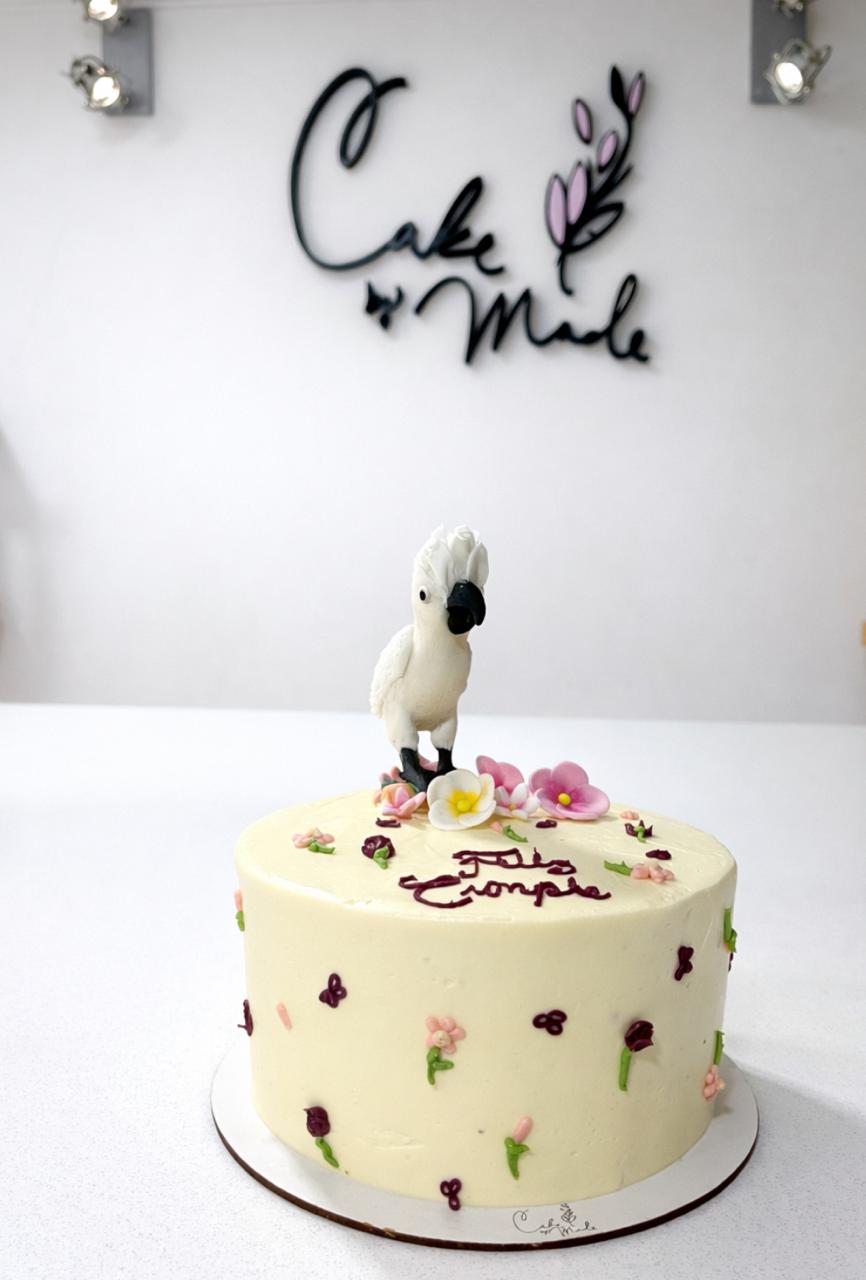 Pastel premium minimalista con escultura realista de ave en fondant y caligrafía manual de "Feliz Cumple".