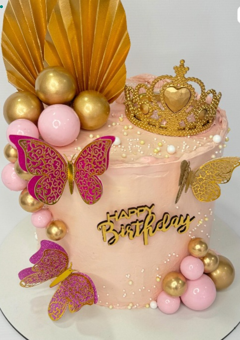 Torta premium rosada con decoración de mariposas caladas fucsia y oro, corona dorada, abanicos plisados y esferas metalizadas.