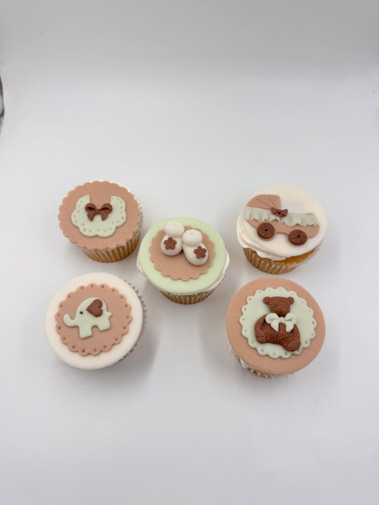 Cupcakes personalizados en Bogotá para baby shower unisex, decorados con cochecito, babero, osito y zapatitos en tonos beige y verde