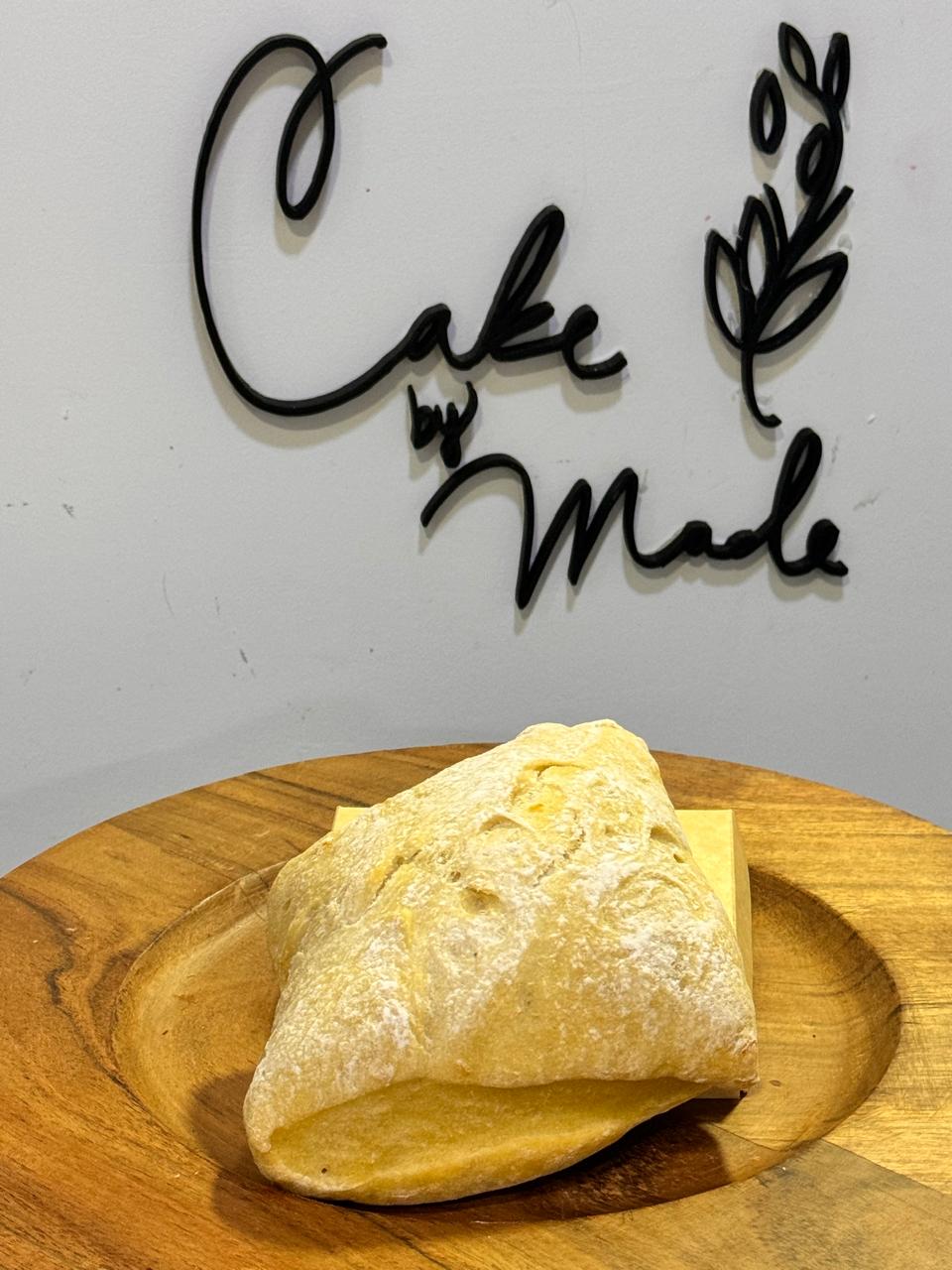 En primer plano se ve un pan de ajo elaborado con masa madre, al fondo se ve un logo desenfocado de >Cake by made