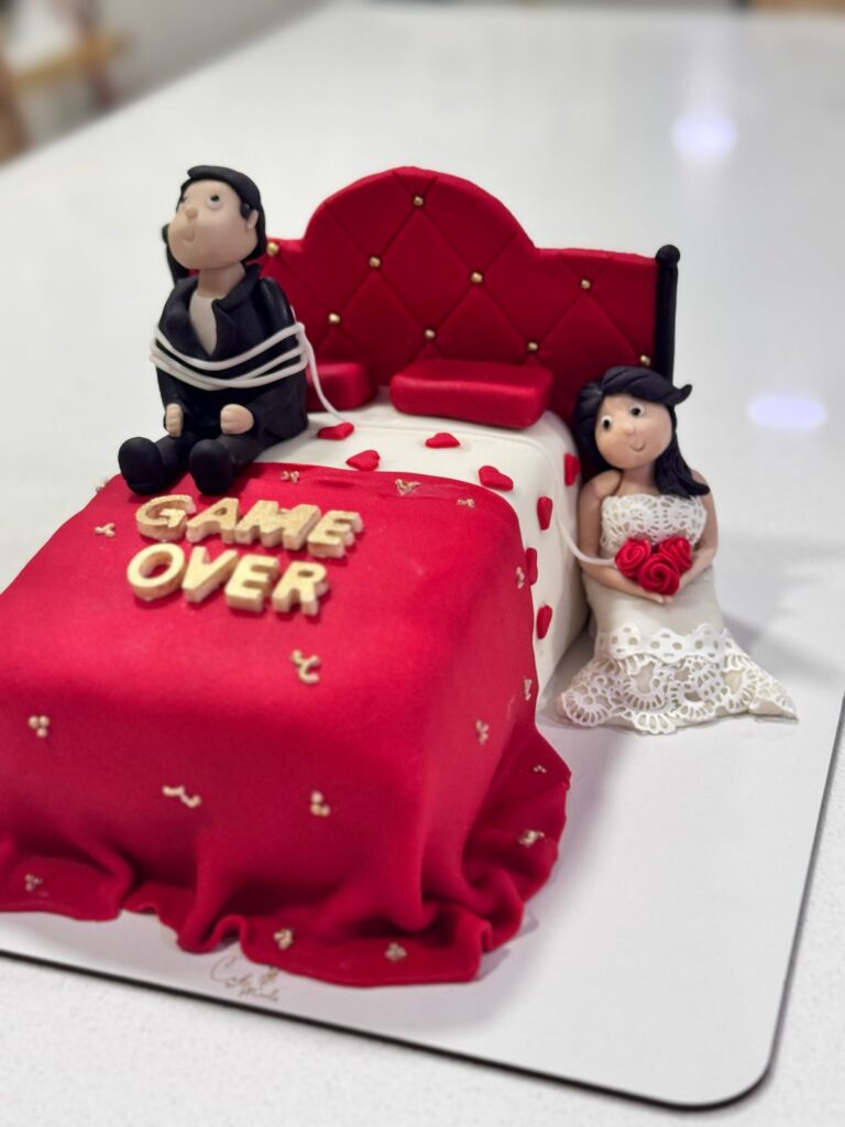 Torta personalizada de matrimonio divertida con figura de novio atado y novia sonriente, decoración en fondant rojo con letras 'Game Over', ideal para bodas originales y pastelería creativa en Bogotá