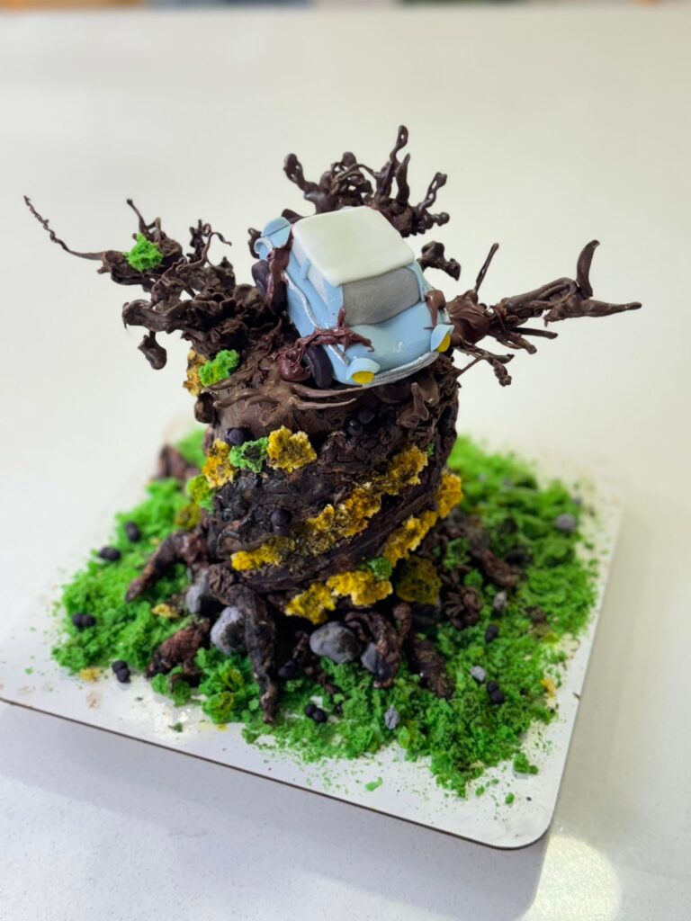 Torta de Harry Potter en Bogotá 4 Primer plano de torta personalizada inspirada en Harry Potter, con diseño de árbol encantado en chocolate, flores comestibles amarillas, raíces detalladas y figura artesanal del Ford Anglia mágico, elaborada por Cake by Made en Bogotá, expertos en pastelería temática y artesanal.