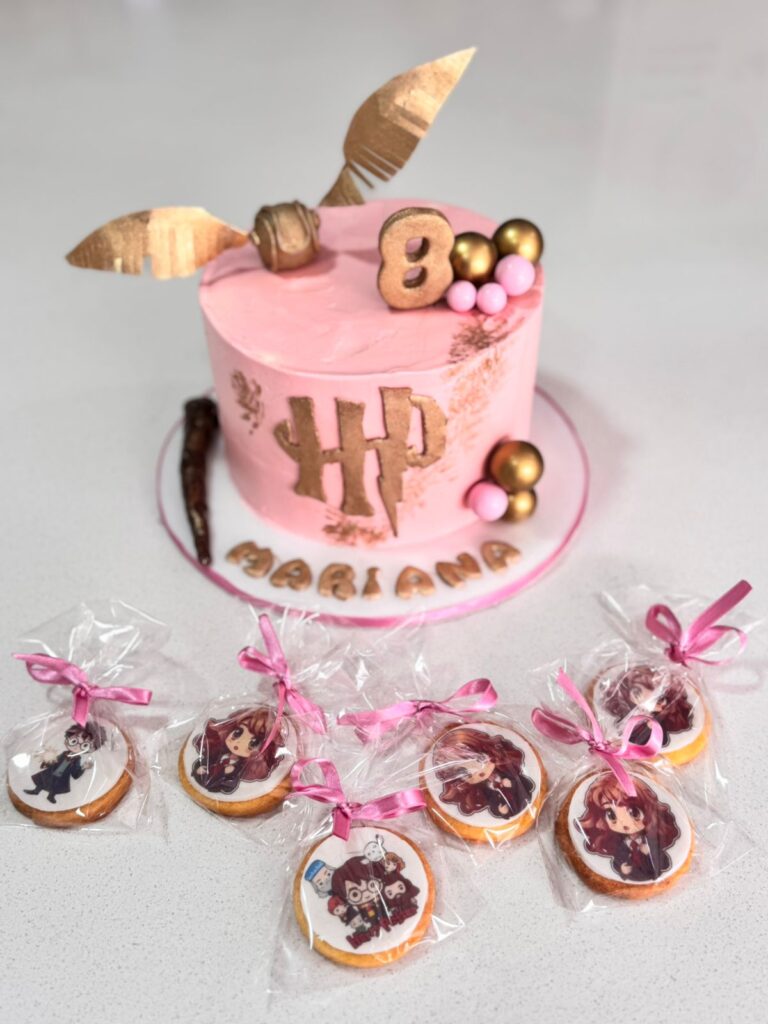 Torta de Harry Potter en Bogotá 5 Torta personalizada inspirada en Harry Potter con cobertura rosa, decorada con Snitch dorada, varita mágica y esferas metálicas, acompañada de galletas artesanales con impresiones comestibles de personajes de la saga, elaboradas por Cake by Made en Bogotá, expertos en pastelería temática y personalizada.