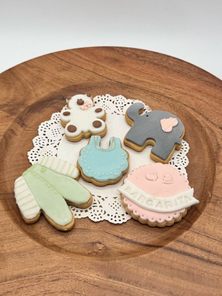 Galletas Personalizadas en Bogotá 82 Decoración de galletas colocadas en un Plato de madera Motivo de baby shower 5 galletas un elefante un delantal un osito un mameluco Y una galleta rosada con el nombre de la niña en fondant