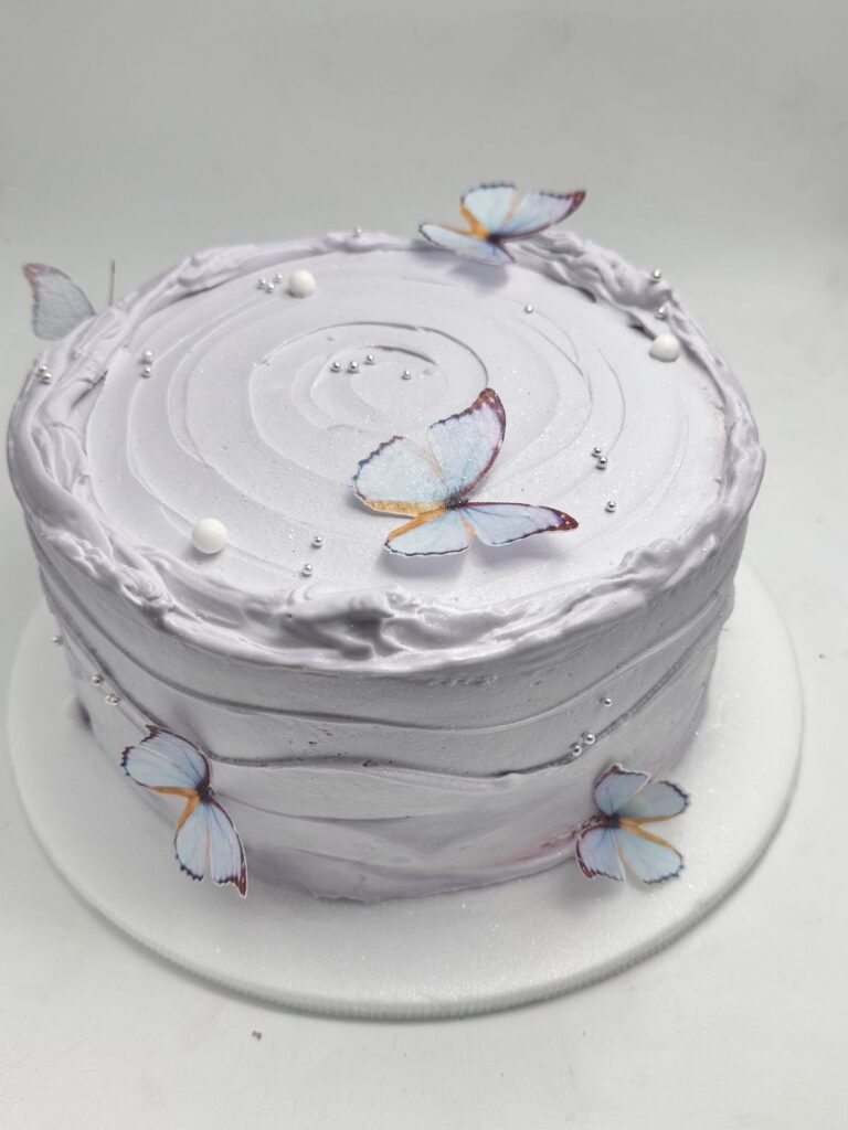 Torta personalizada en crema blanca con mariposas comestibles en tonos azules y decoraciones plateadas, ideal para cumpleaños, celebraciones especiales y eventos elegantes en Bogotá"