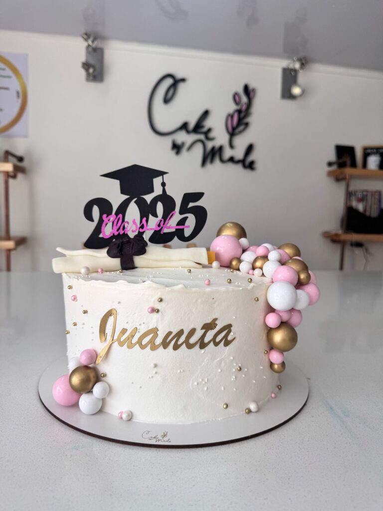 "Torta personalizada de grado 2025 en crema blanca con decoración de perlas doradas, rosadas y blancas, topper con birrete y nombre Juanita, ideal para celebraciones de graduación en Bogotá"