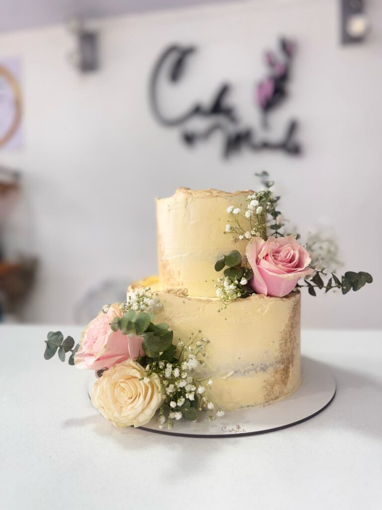 "Elegante pastel de dos pisos para bodas, decorado con rosas rosadas y crema, eucalipto y gypsophila. Diseño rústico chic, ideal para eventos especiales en Bogotá. Pastelería personalizada."