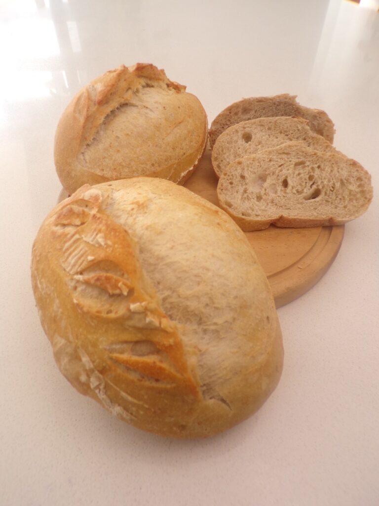 Panes artesanales de centeno con masa madre, enteros y rebanados, sobre tabla de madera en superficie clara, elaborados en Cake by Made, panadería saludable en Bogotá