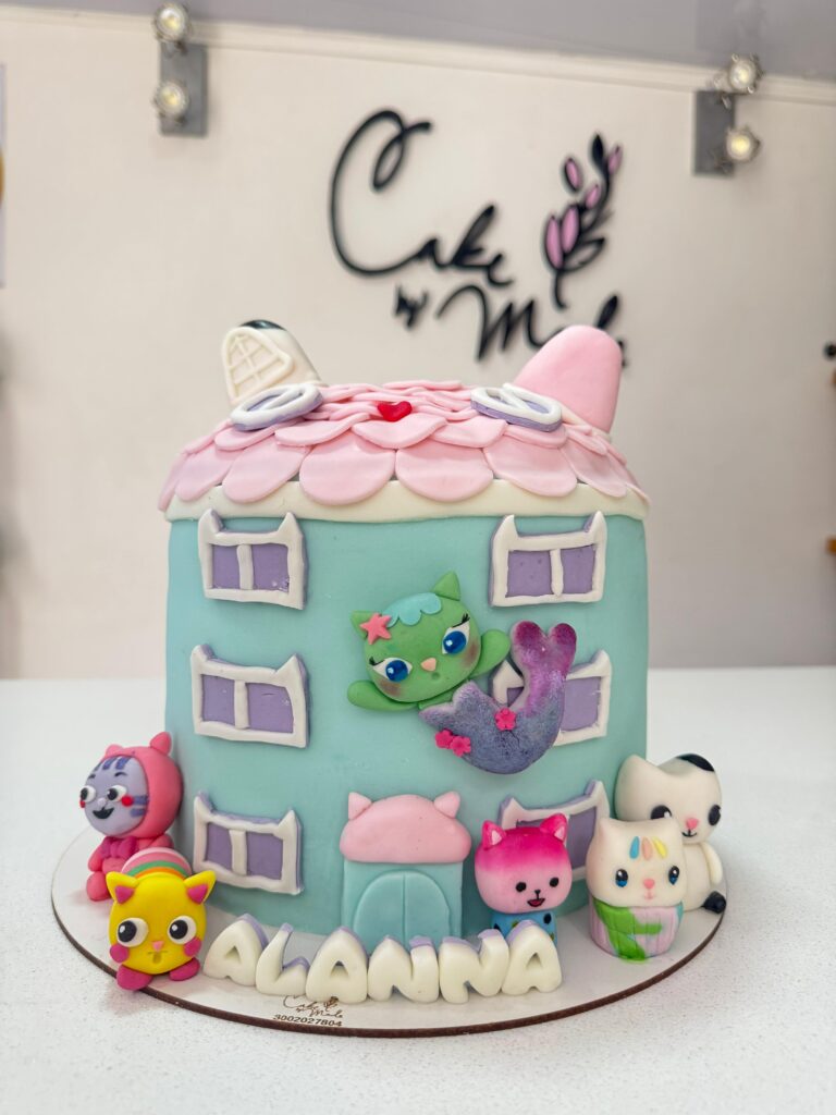 Encantadora torta personalizada inspirada en Gabby’s Dollhouse, con diseño en forma de casa, techo rosado, ventanas en fondant y figuras de personajes adorables. Incluye nombre personalizado y es perfecta para sorprender en cumpleaños de niñas fanáticas de la serie. Disponible en Cake by Made, pastelería creativa en Bogotá.