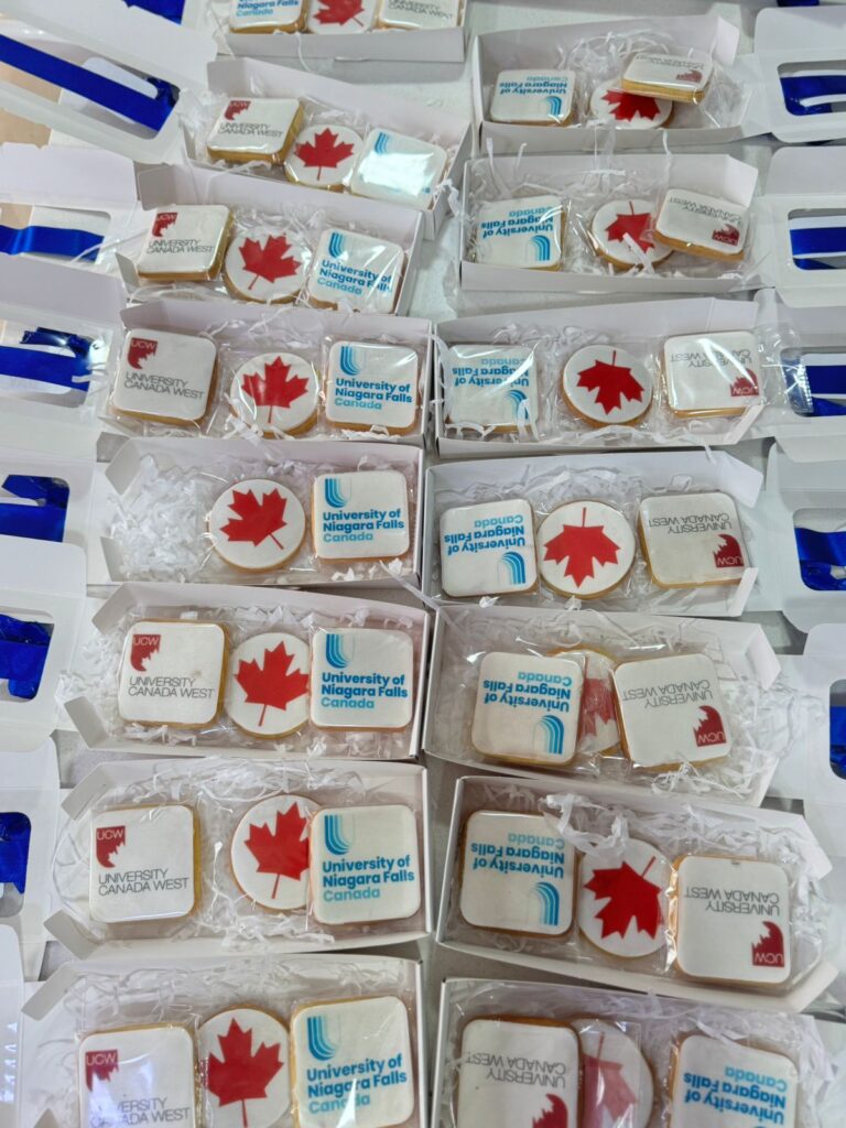 Galletas Personalizadas en Bogotá 21 "Cajas con galletas corporativas personalizadas para University Canada West y University of Niagara Falls Canada, decoradas con logos institucionales y hoja de arce, ideales para celebraciones internacionales como el Día de Canadá, elaboradas en Bogotá."