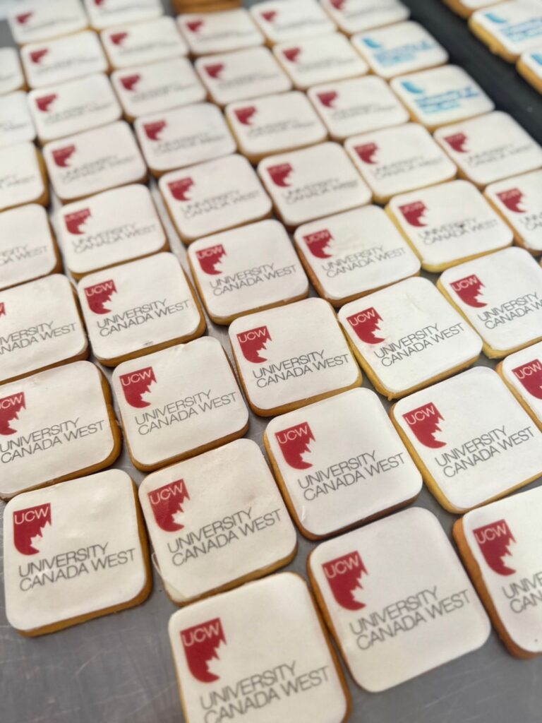 Galletas Personalizadas en Bogotá 11 "Galletas corporativas cuadradas personalizadas con el logo de University Canada West, ideales para eventos institucionales, ferias académicas y estrategias de promoción educativa en Bogotá."