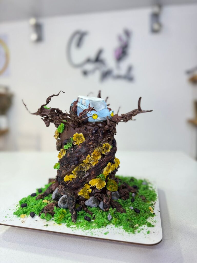 Tortas Personalizadas en Bogotá 35 Torta personalizada inspirada en Harry Potter, con diseño de árbol encantado, flores comestibles y una figura temática de carro mágico, elaborada artesanalmente por Cake by Made en Bogotá, expertos en pastelería creativa para ocasiones especiales.