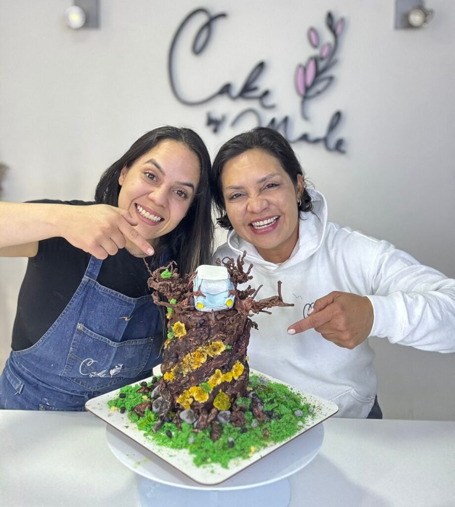 Torta de Harry Potter en Bogotá 3 Dos pasteleras sonrientes presentan una torta personalizada con diseño de árbol encantado, decorada con flores comestibles y figuras temáticas, en Cake by Made, pastelería artesanal en Bogotá especializada en tortas únicas para ocasiones especiales.