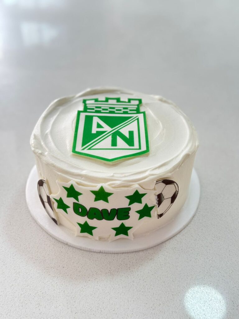 Tortas Personalizadas en Bogotá 55 Torta personalizada en crema blanca con el escudo del Atlético Nacional en la parte superior, decorada con estrellas verdes, balones de fútbol y el nombre Dave. Pastel artesanal ideal para hinchas del fútbol colombiano, elaborado por Cake by Made en Bogotá."
